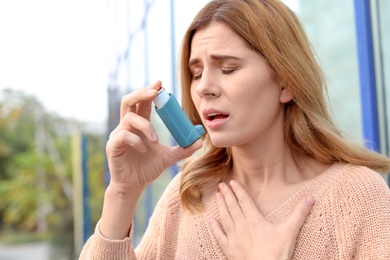 Photo of Woman using asthma inhaler outdoors. Health care