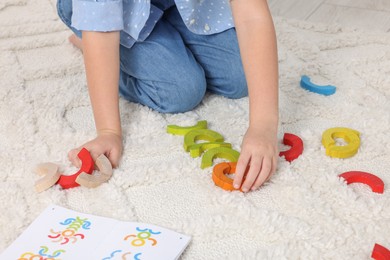 Motor skills development. Girl playing with colorful wooden arcs on carpet, closeup