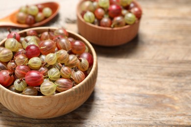 Photo of Bowls of fresh ripe gooseberries on wooden table, closeup. Space for text