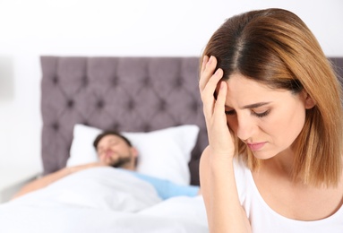 Photo of Upset woman sitting on bed near her sleeping husband at home. Relationship problems