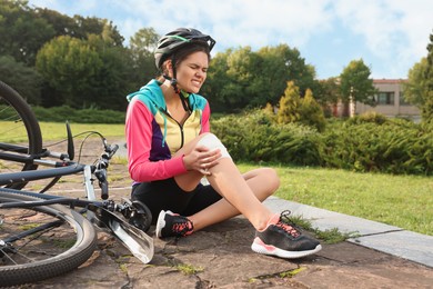 Photo of Young woman with injured knee near bicycle outdoors