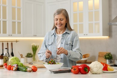 Photo of Happy woman making salad at table in kitchen