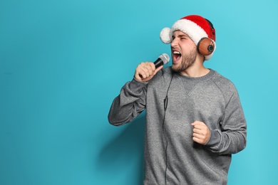Photo of Young man in Santa hat singing into microphone on color background. Christmas music