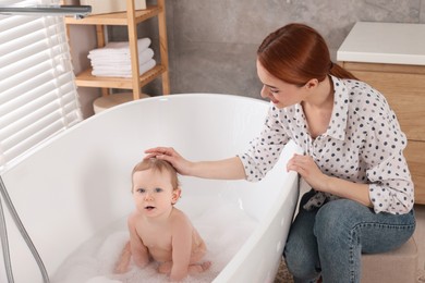 Photo of Mother washing her little baby in tub at home