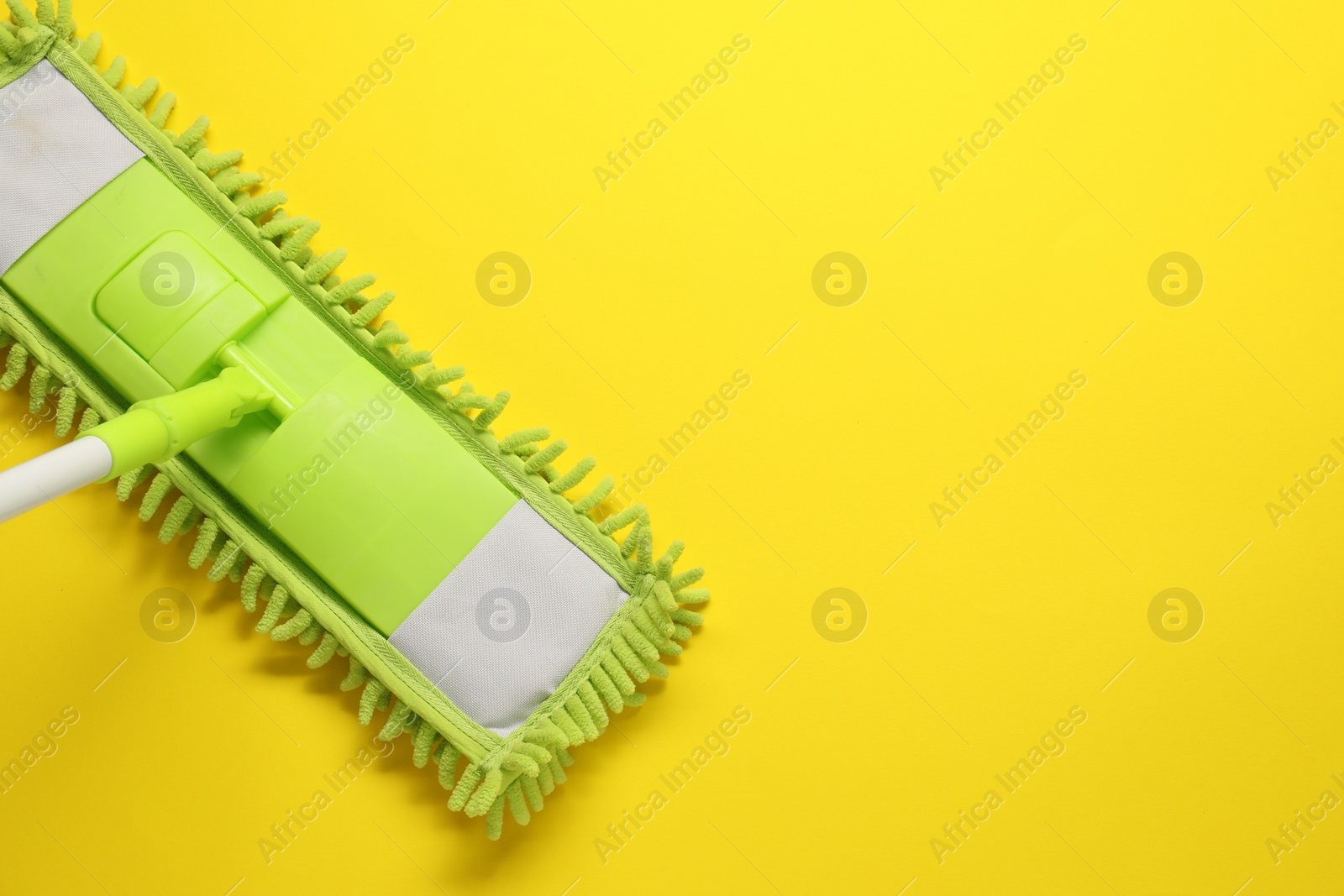 Photo of Mop with plastic handle on yellow background, top view. Space for text