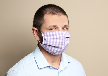 Photo of Man wearing handmade cloth mask on beige background. Personal protective equipment during COVID-19 pandemic