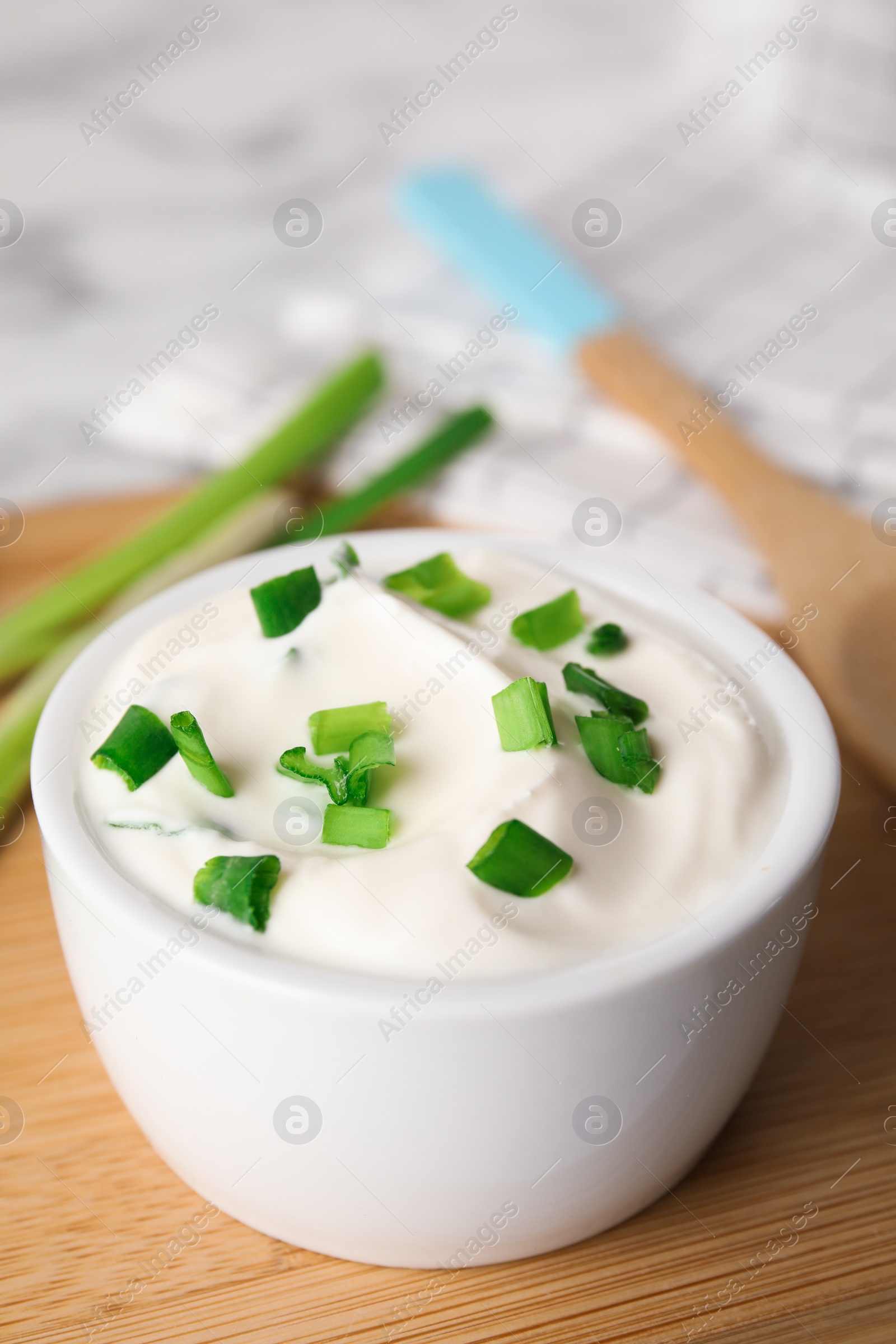 Photo of Fresh sour cream with onion on wooden board, closeup