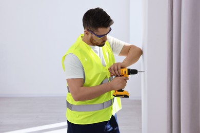 Photo of Young worker in uniform using electric drill indoors