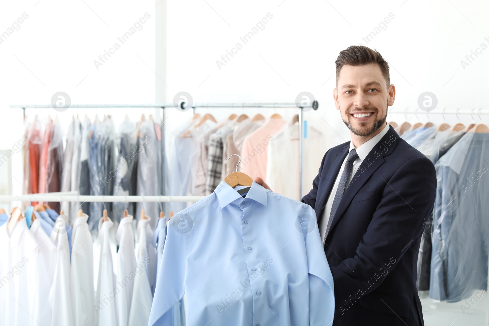 Photo of Young businessman holding hanger with shirt at dry-cleaner's