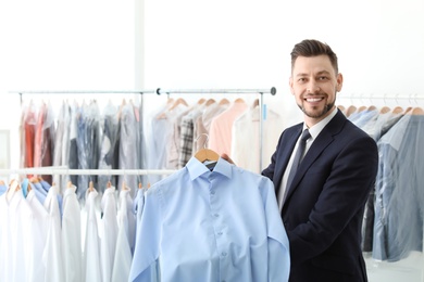 Young businessman holding hanger with shirt at dry-cleaner's