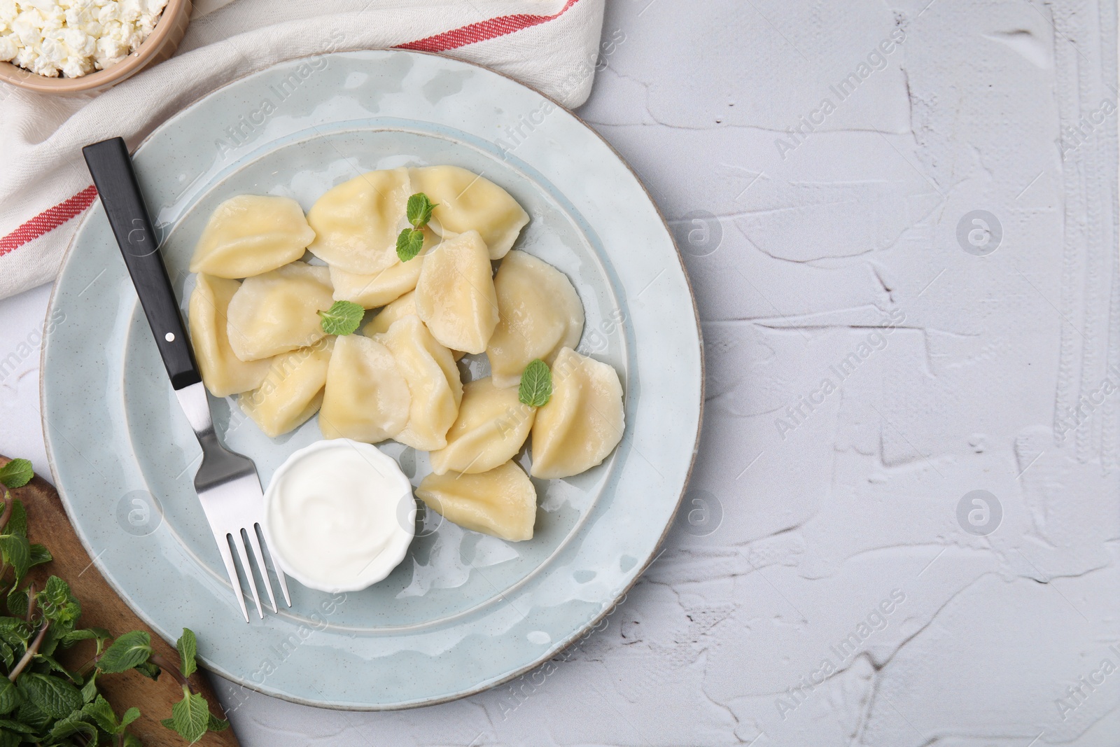 Photo of Delicious dumplings (varenyky) with cottage cheese mint and sour cream served on white table, flat lay. Space for text