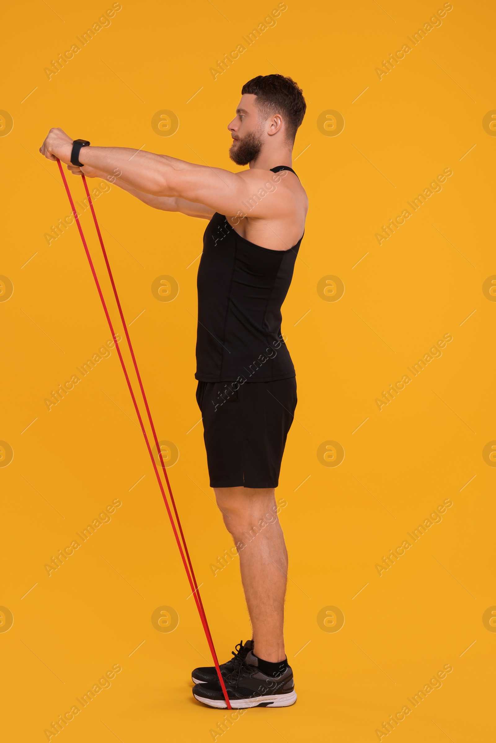 Photo of Young man exercising with elastic resistance band on orange background