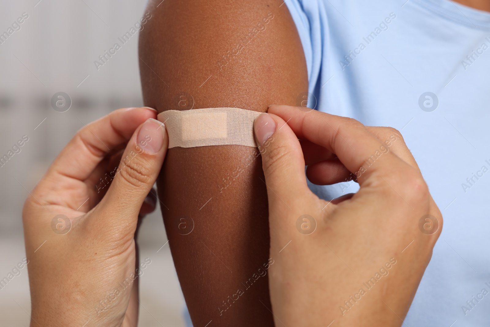 Photo of Doctor putting adhesive bandage on young woman's arm after vaccination indoors, closeup