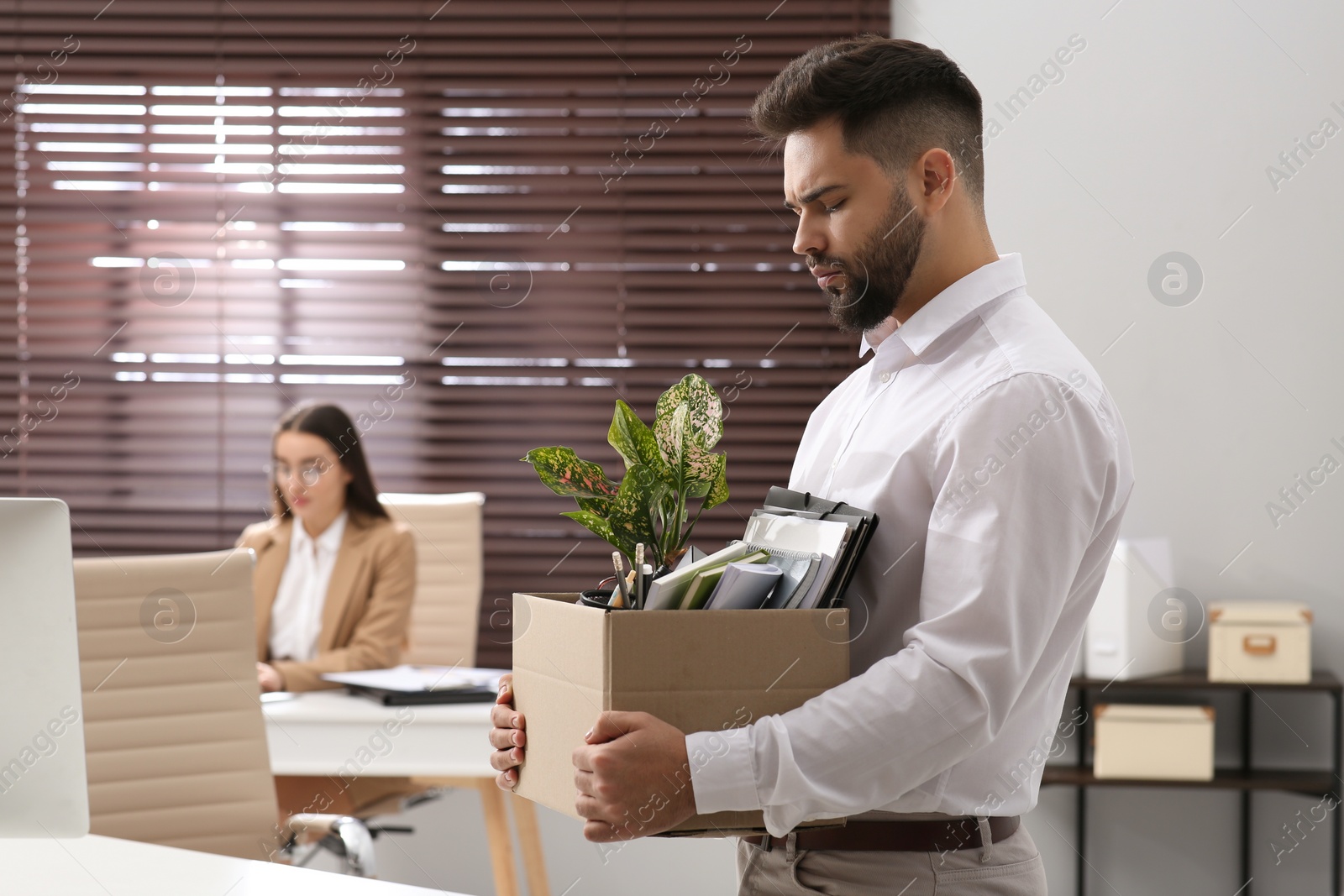 Photo of Upset dismissed man carrying box with personal stuff in office