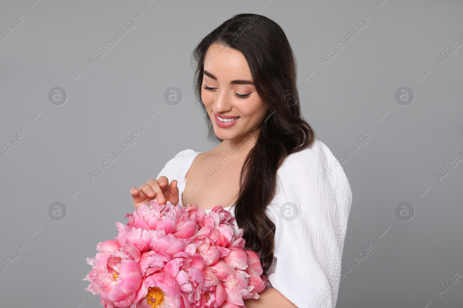 Photo of Beautiful young woman with bouquet of pink peonies on grey background