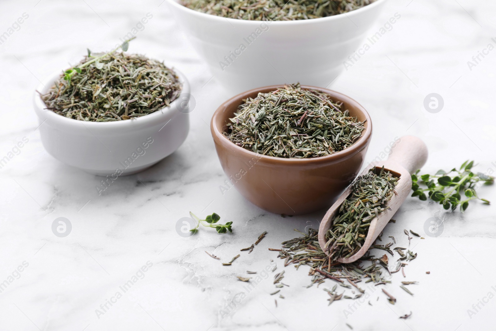 Photo of Bowls and scoop with dried thyme on white marble table, closeup