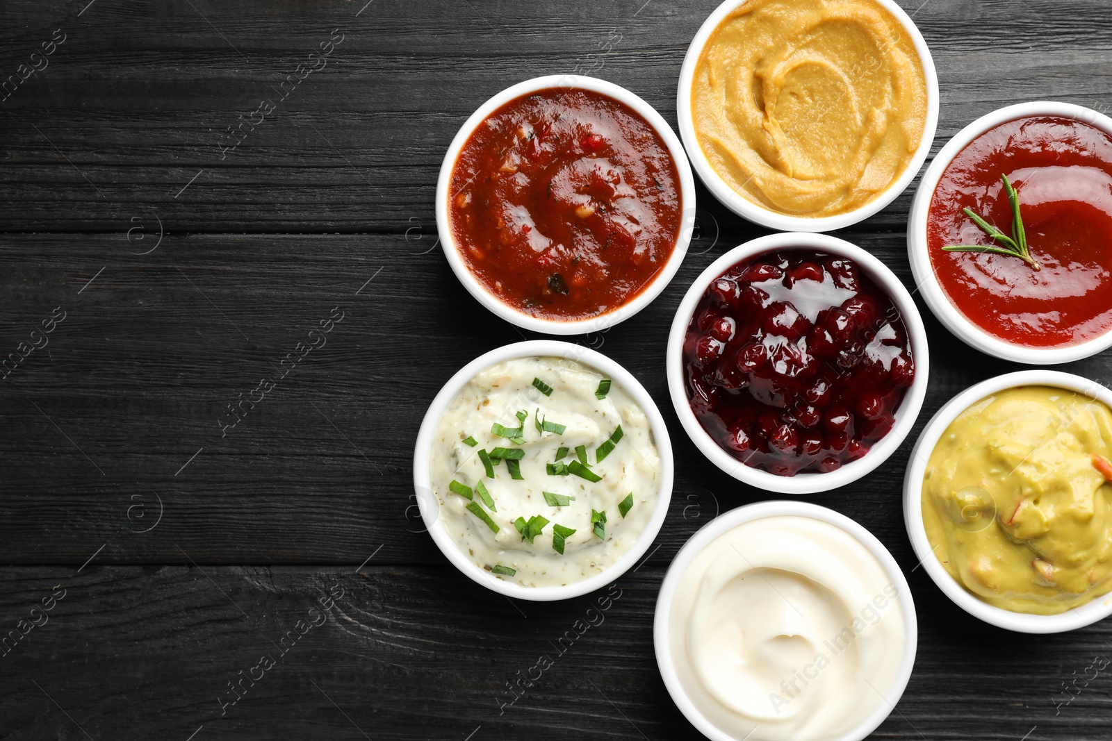 Photo of Different tasty sauces in bowls on black wooden table, flat lay. Space for text