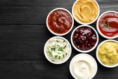 Different tasty sauces in bowls on black wooden table, flat lay. Space for text