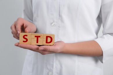 Photo of Doctor holding wooden cubes with abbreviation STD on white background, closeup