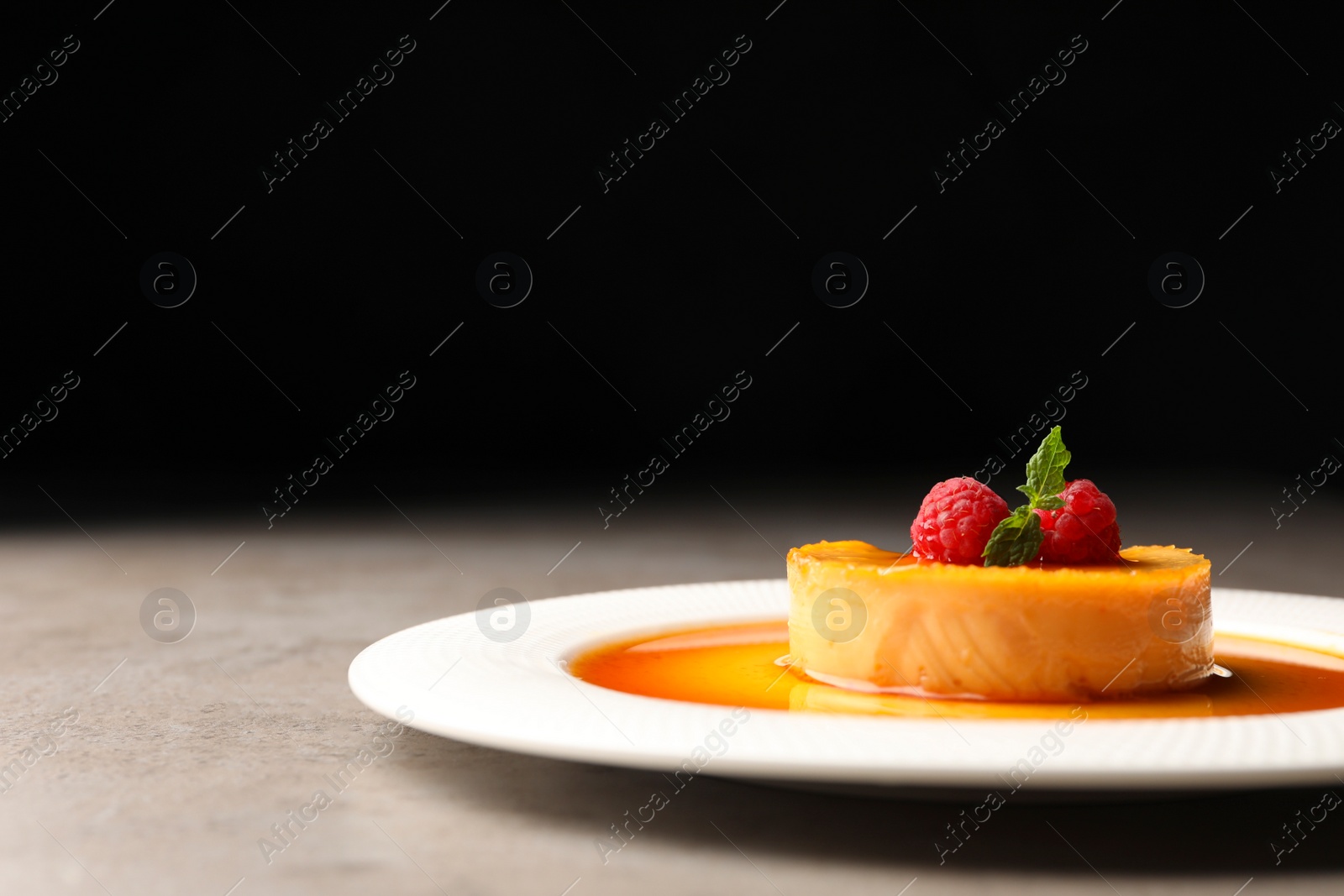 Photo of Delicious pudding with caramel and raspberries on grey table against black background. Space for text