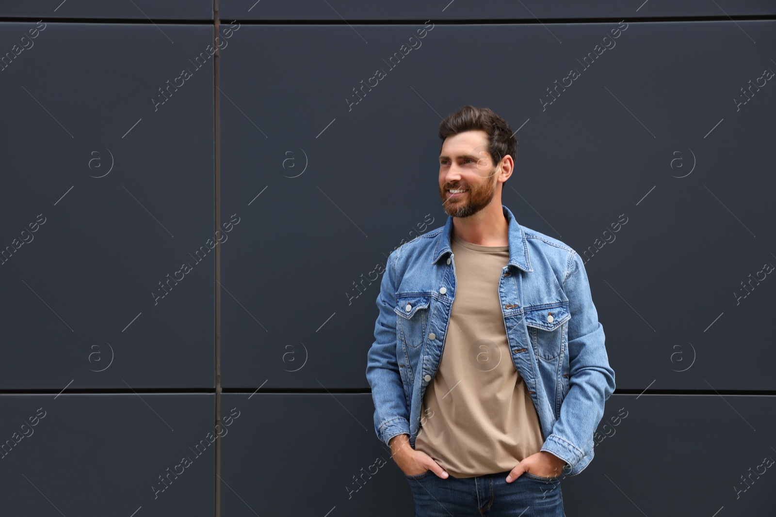 Photo of Smiling handsome bearded man near grey wall outdoors. Space for text