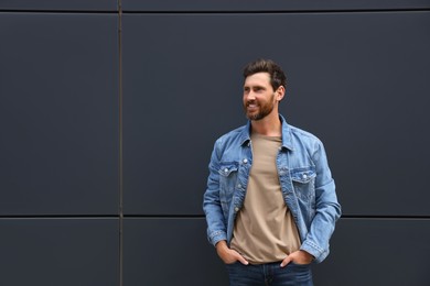 Photo of Smiling handsome bearded man near grey wall outdoors. Space for text