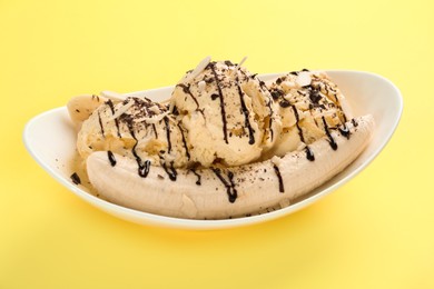 Photo of Delicious banana split ice cream with toppings on yellow background