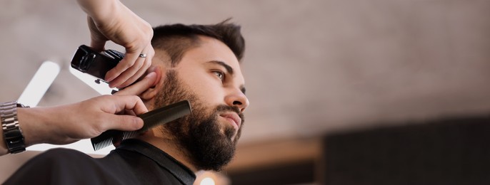 Image of Professional hairdresser working with bearded client in barbershop, low angle view and space for text. Banner design