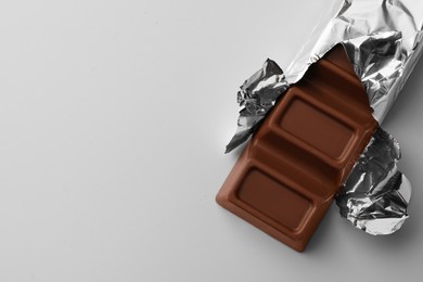 Photo of Delicious chocolate bar wrapped in foil on light blue background, top view. Space for text