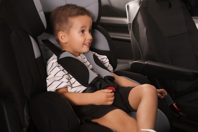 Photo of Little boy fastened with car safety belt in child seat