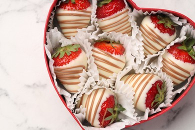 Photo of Heart shaped box with delicious chocolate covered strawberries on white marble table, top view