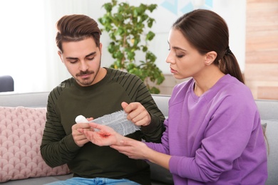 Young man applying bandage on woman's injured hand at home. First aid