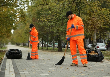 Photo of Street cleaners sweeping fallen leaves outdoors on autumn day