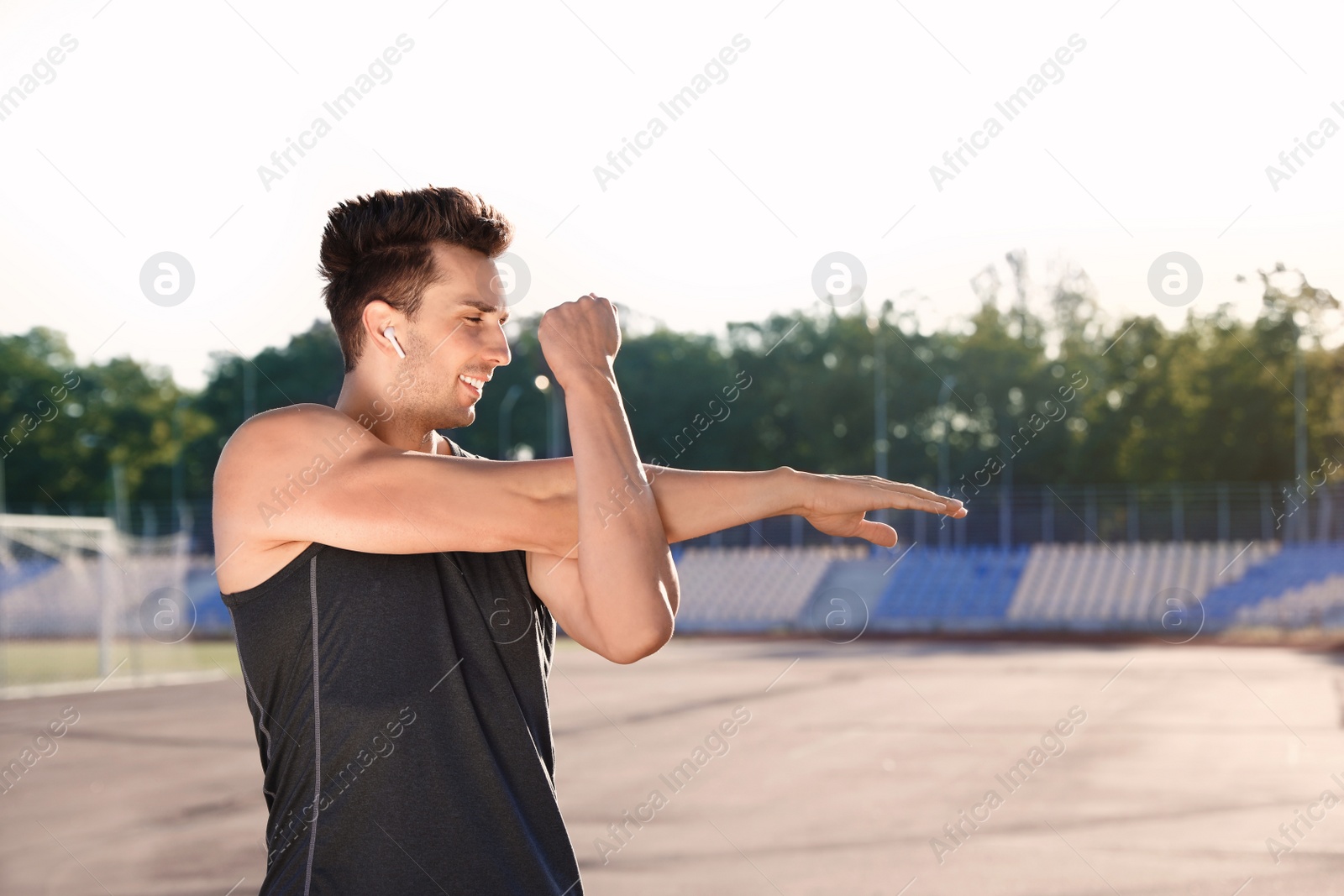 Photo of Young sportsman with wireless earphones stretching at stadium