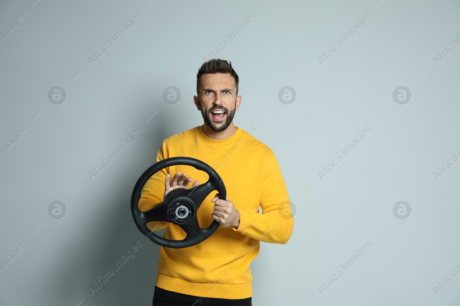 Photo of Emotional man with steering wheel on grey background