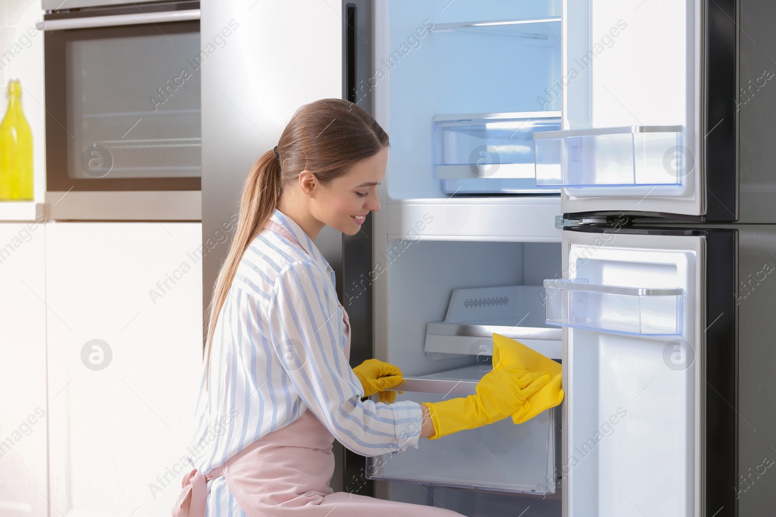 Photo of Woman in rubber gloves cleaning refrigerator at home