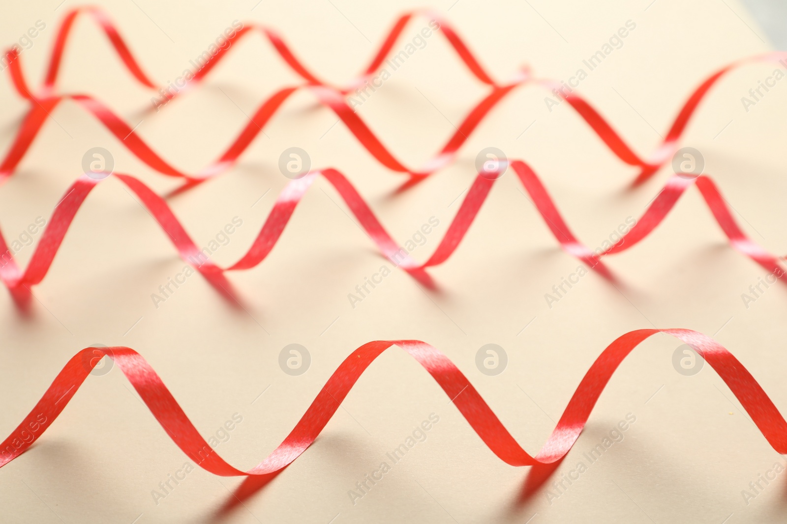 Photo of Shiny red serpentine streamers on beige background, closeup