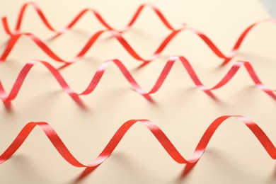 Shiny red serpentine streamers on beige background, closeup