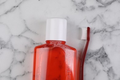 Photo of Fresh mouthwash in bottle and toothbrush on white marble table, top view