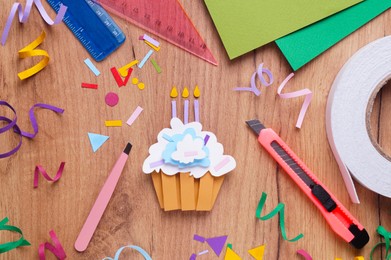 Photo of Paper cupcake, confetti and stationery on wooden table, flat lay
