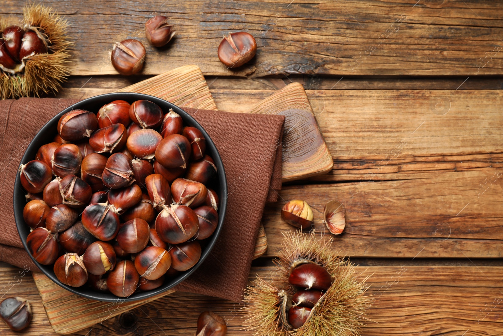 Photo of Delicious roasted edible chestnuts on wooden table, flat lay. Space for text