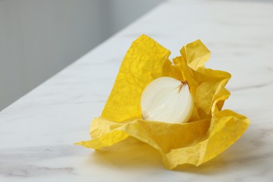 Half of onion with yellow beeswax food wrap on white marble table, closeup. Space for text