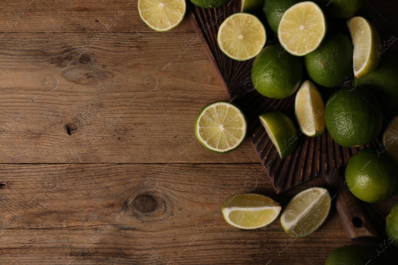 Photo of Fresh whole and cut limes on wooden table, flat lay. Space for text