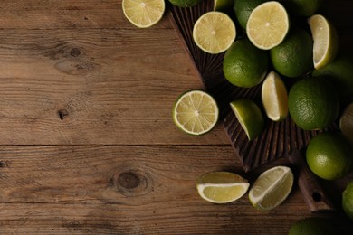 Photo of Fresh whole and cut limes on wooden table, flat lay. Space for text