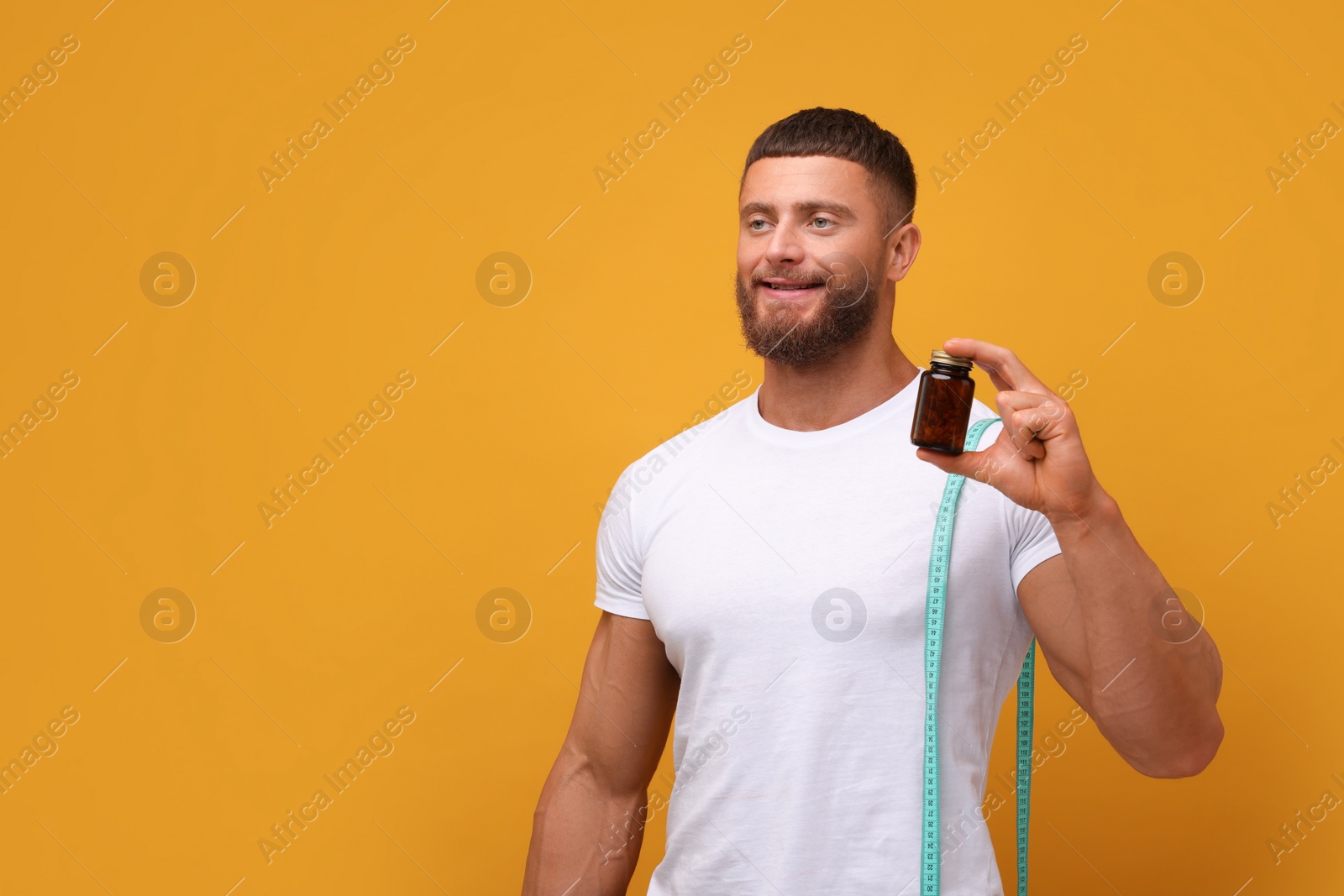 Photo of Athletic young man with measuring tape and bottle of supplements on orange background, space for text. Weight loss