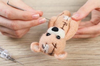 Photo of Woman felting cute toy bear from wool at wooden table, closeup