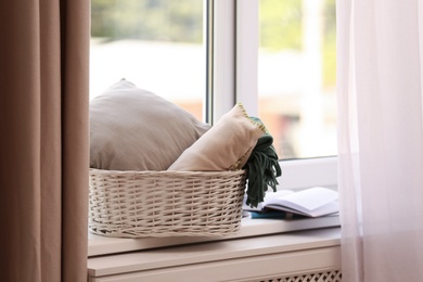Photo of Basket with blankets and pillow on windowsill indoors