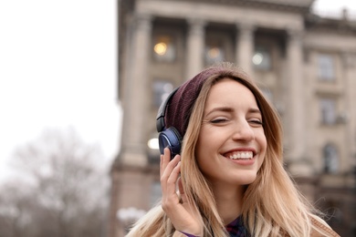 Photo of Young woman with headphones listening to music outdoors. Space for text