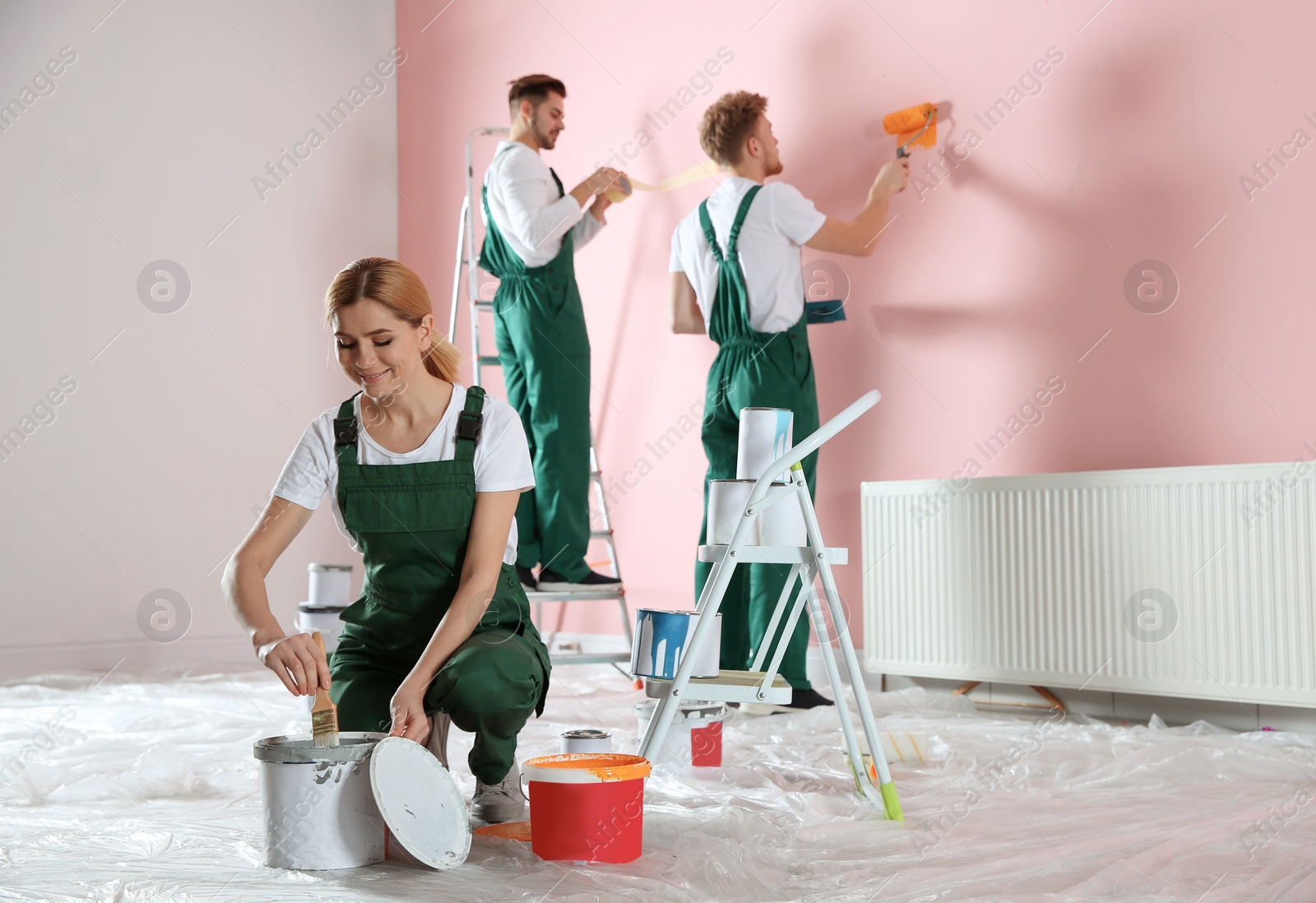 Photo of Team of professional decorators painting wall indoors. Home repair service