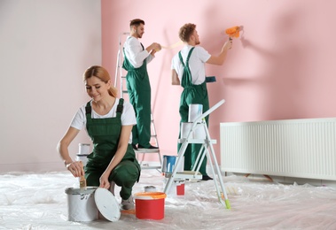 Photo of Team of professional decorators painting wall indoors. Home repair service